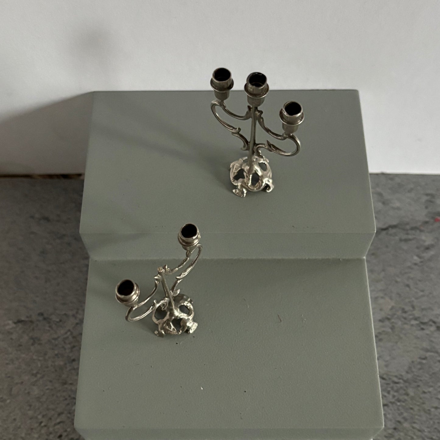 Two silver candelabra with skull designs on a white stand against a light gray background.