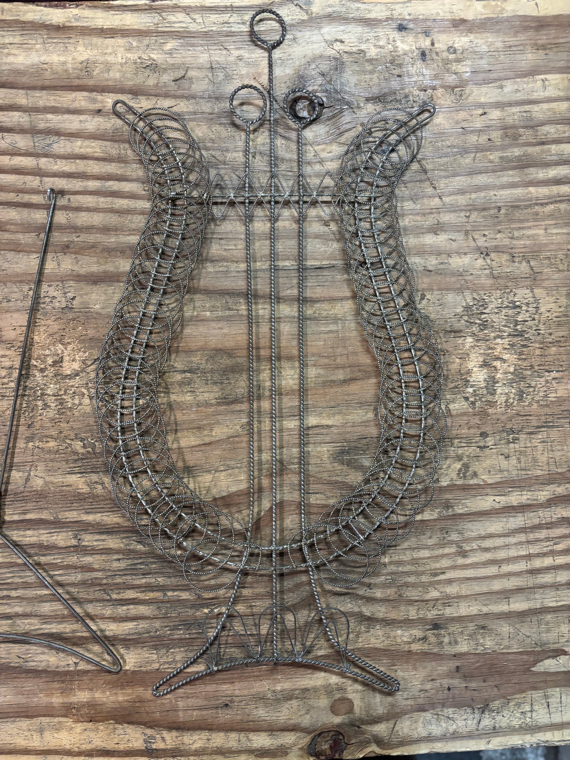 A rustic metal wire lyre wall hanging displayed on a weathered wooden plank background.