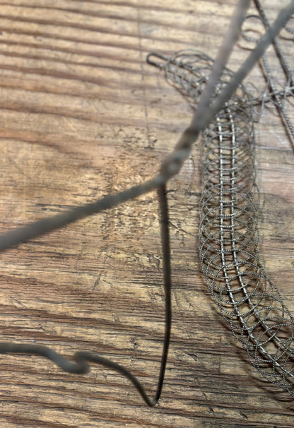 A close-up of a dark metal wire frame or cage structure resting on a weathered, textured wooden surface.