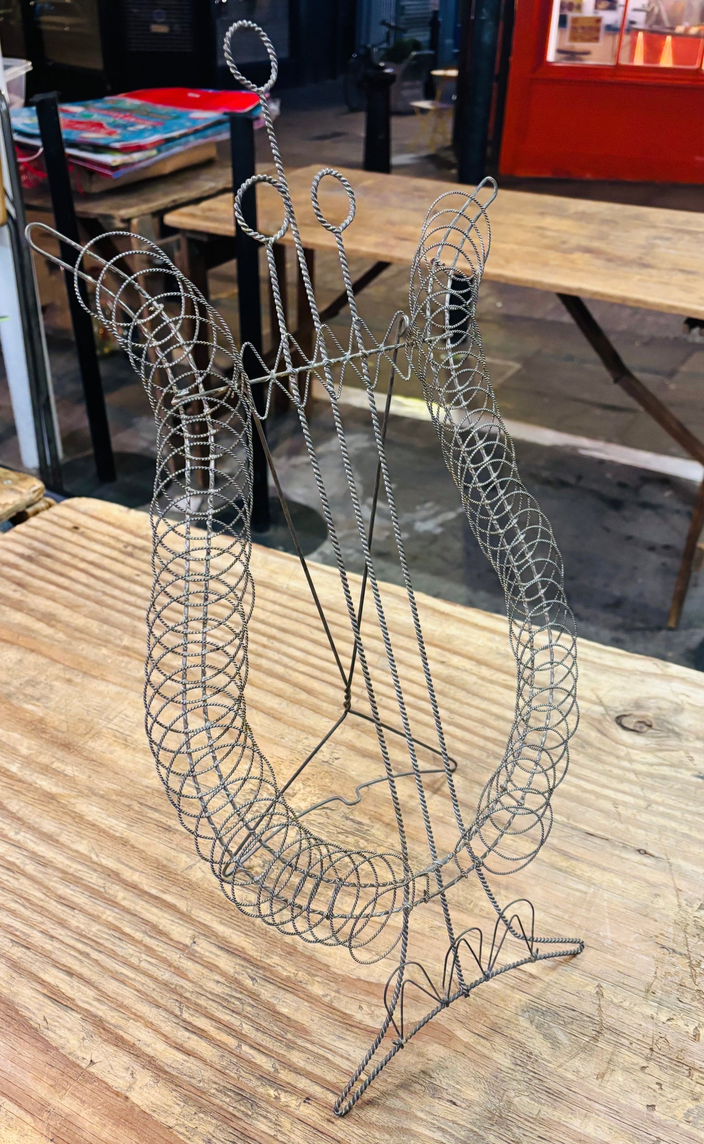 A silver metal wire wine bottle holder with a spiral cage design and a central stand, displayed on a rustic wooden table.