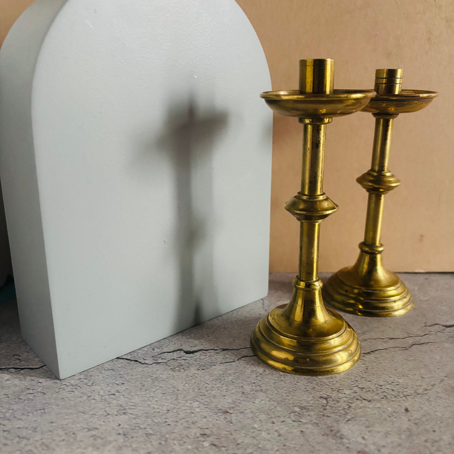 Two brass candle holders on a textured surface with a neutral background