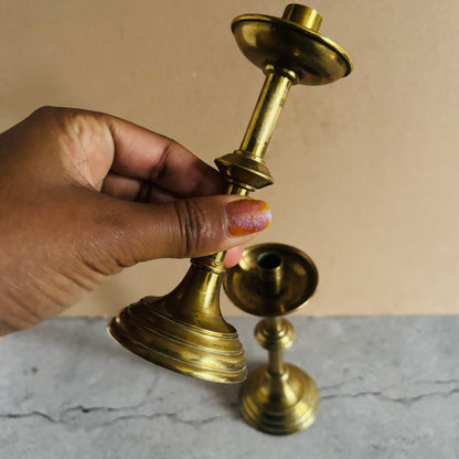 Hand holding two brass candle holders on a marble surface with a beige background