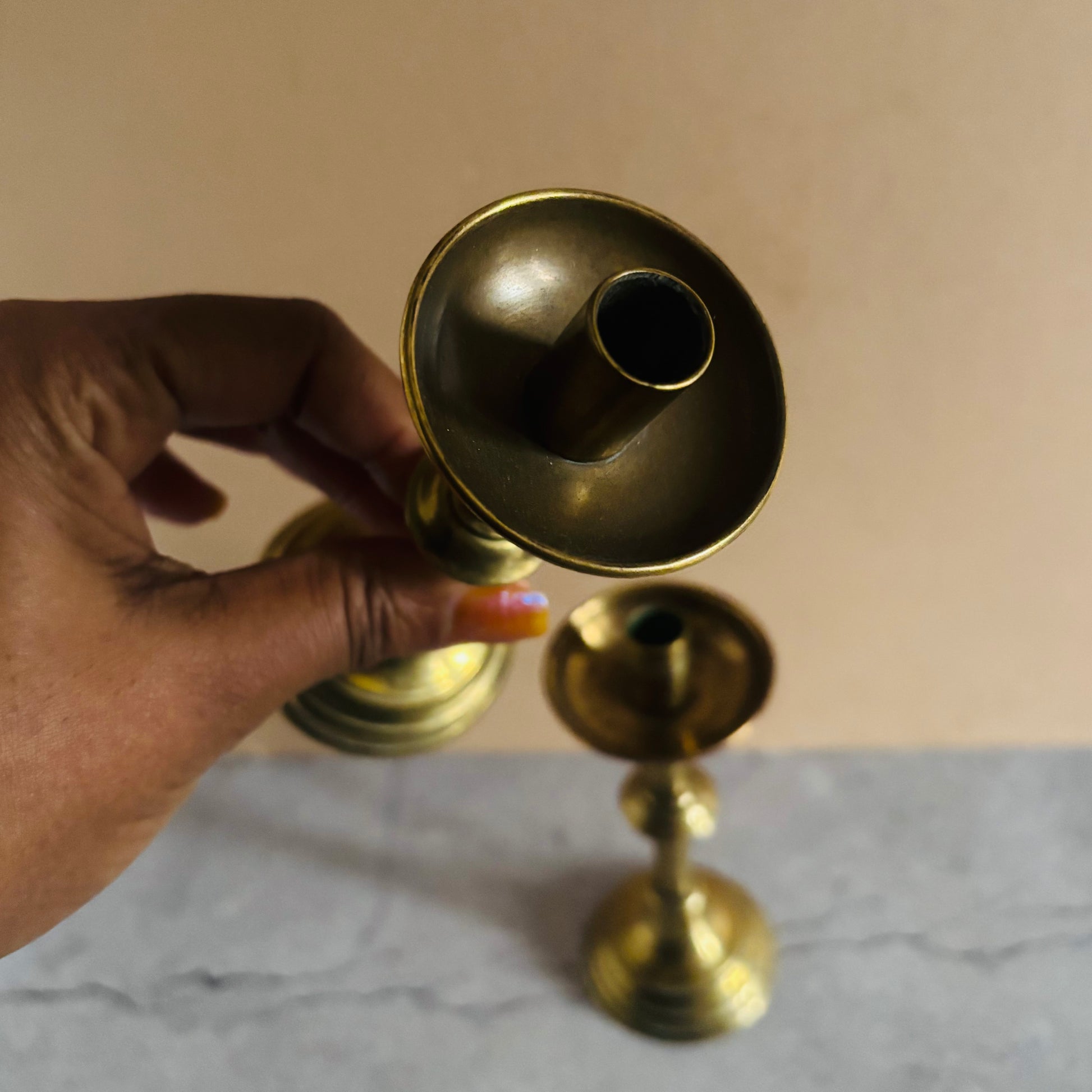 Brass candle holder held by a hand on a neutral background