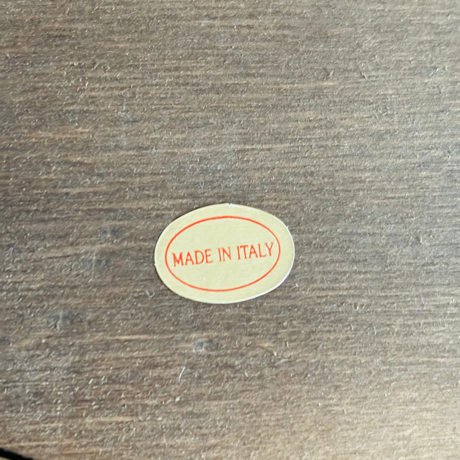 Small oval 'MADE IN ITALY' sticker on a wooden surface