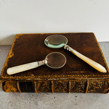 Two vintage magnifying glasses on an old book with a white background