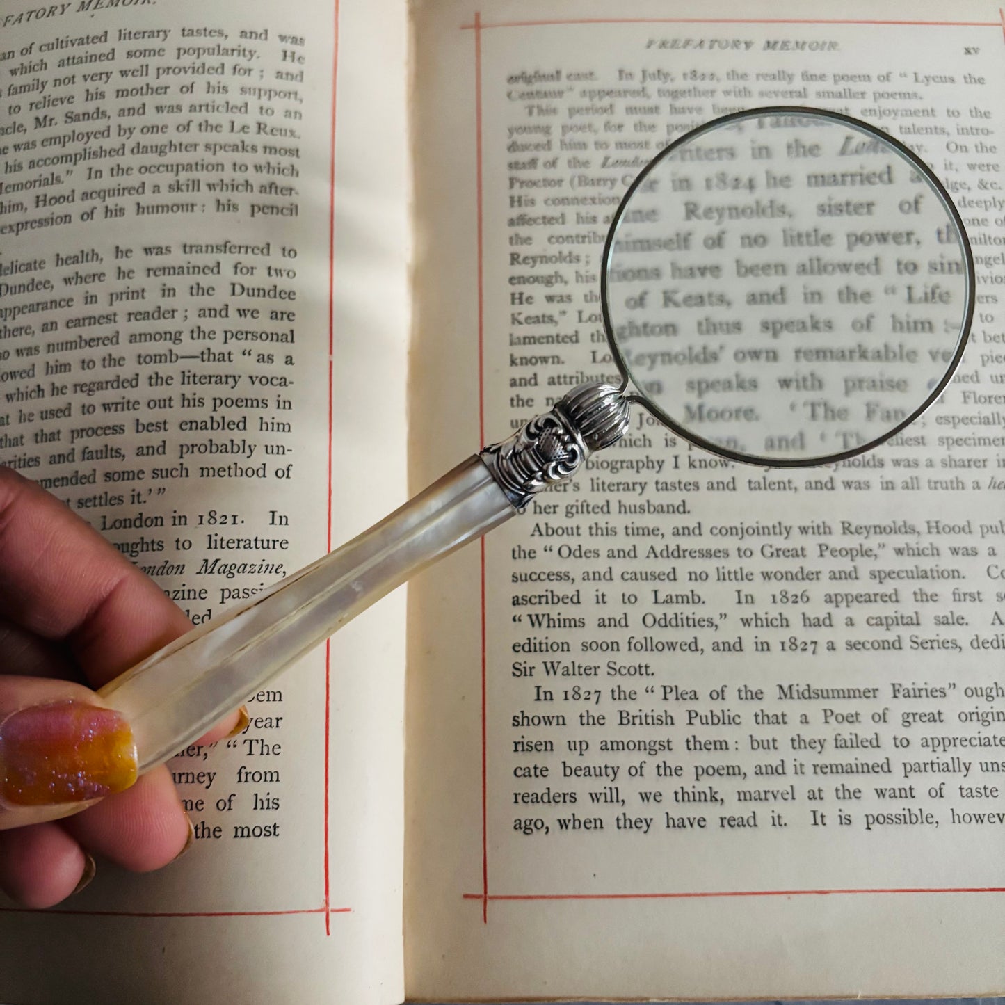 Hand holding a magnifying glass over an open book