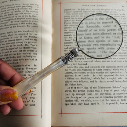 Hand holding a magnifying glass over an open book