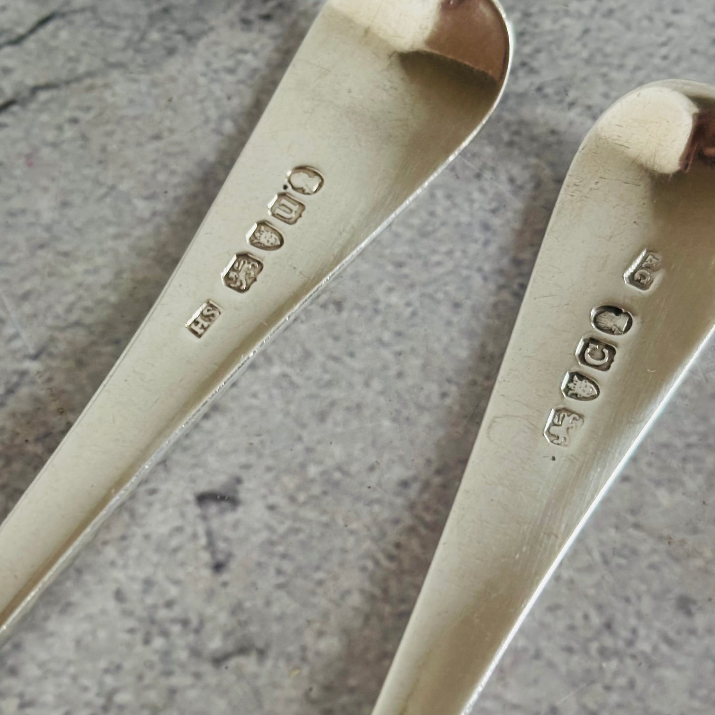 Two sterling silver spoons with engraved Georgian hallmarks marks on a textured surface