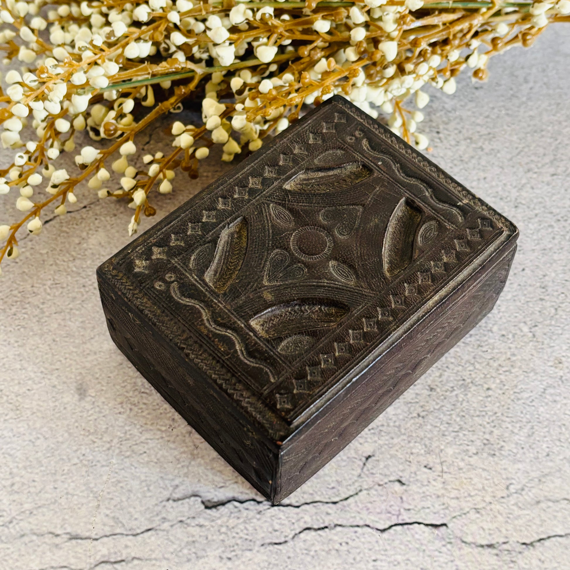 Decorative leather box with intricate carvings on a textured surface with flowers in the background
