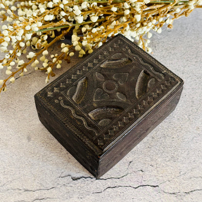 Decorative leather box with intricate carvings on a textured surface with flowers in the background