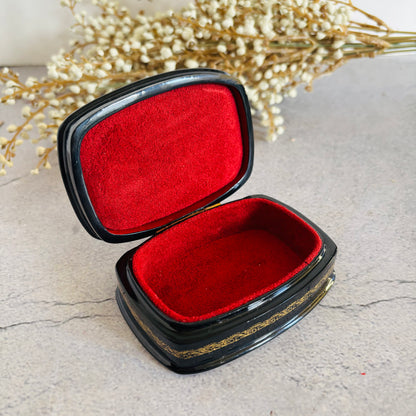Black jewelry box with red interior on a light surface with dried flowers in the background
