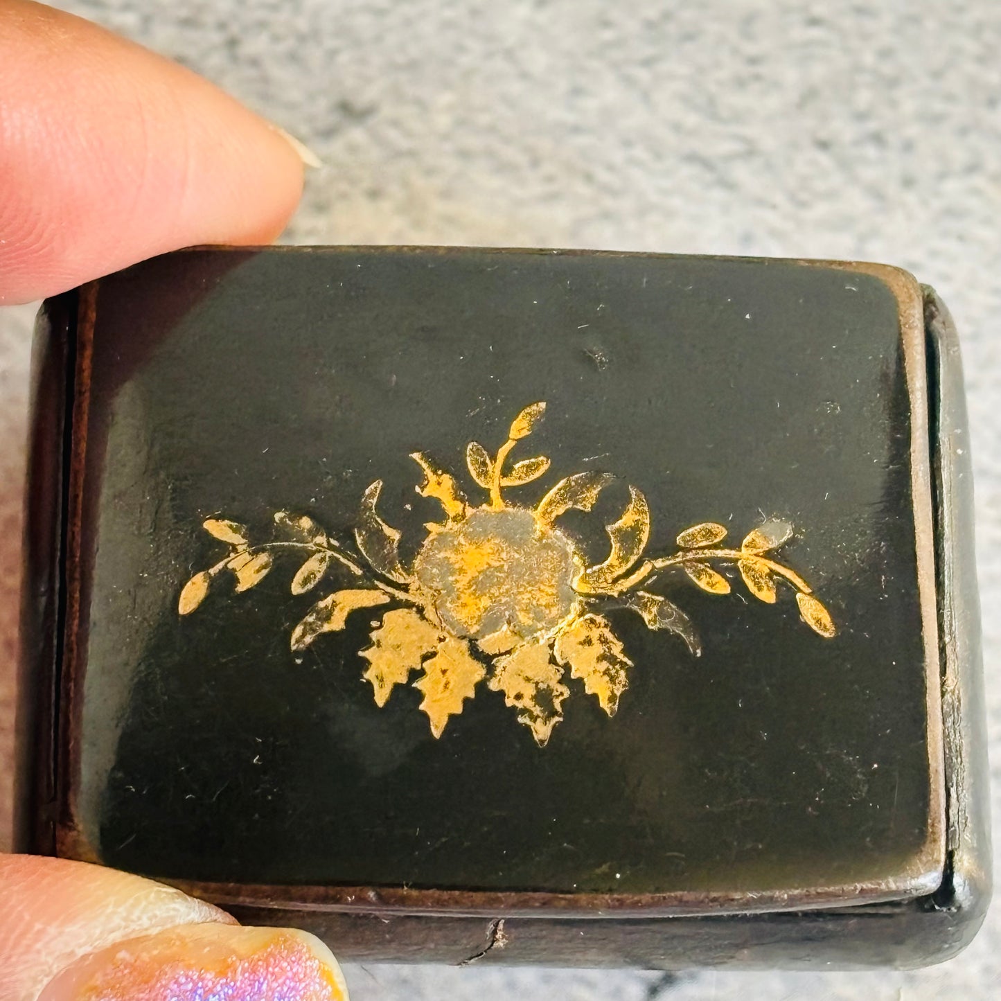 Small black box with gold floral design held by a hand