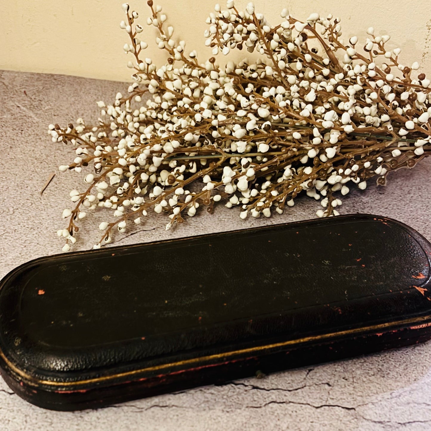 Black rectangular object on a textured surface with dried flowers above