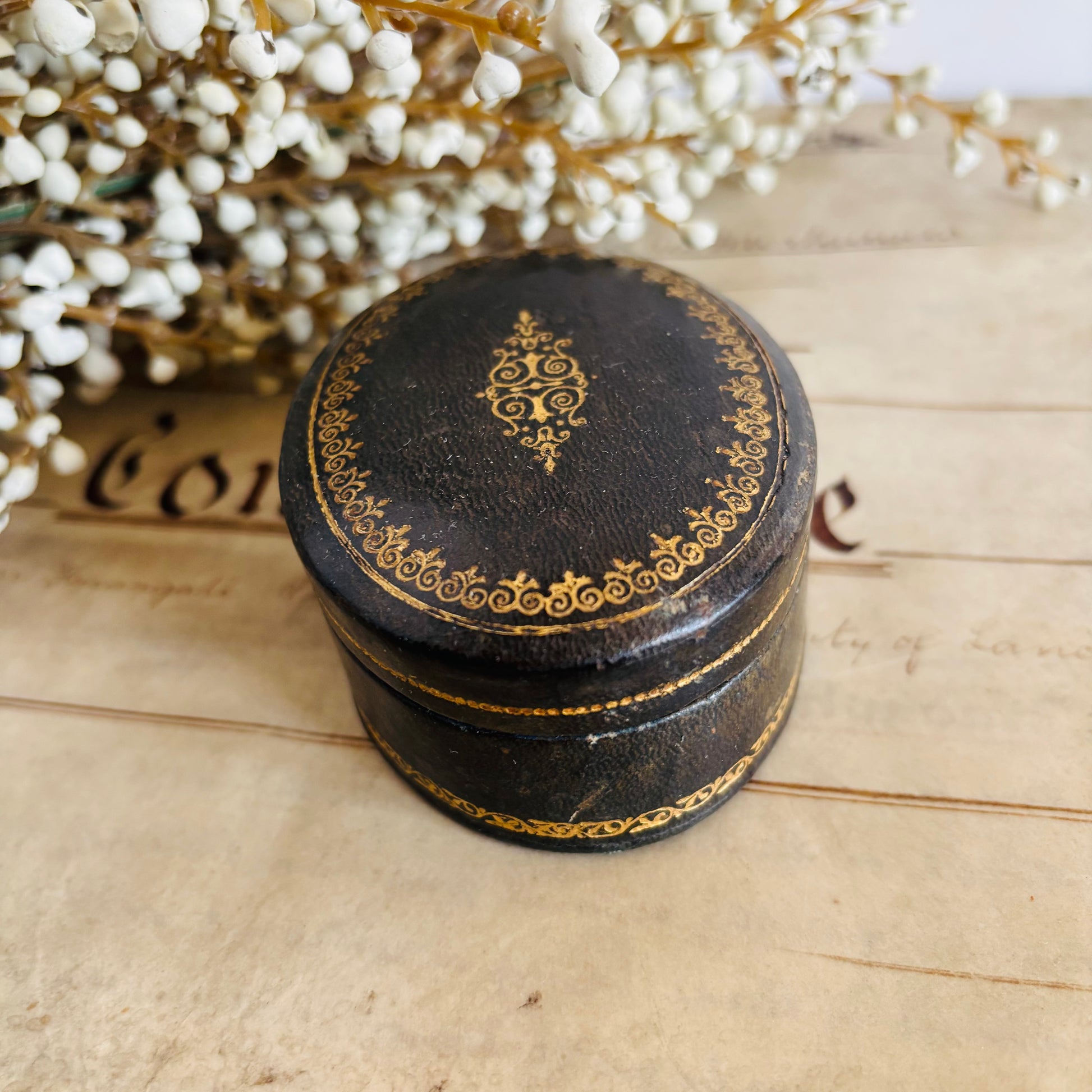 Decorative black round box with gold patterns with white flowers in the background