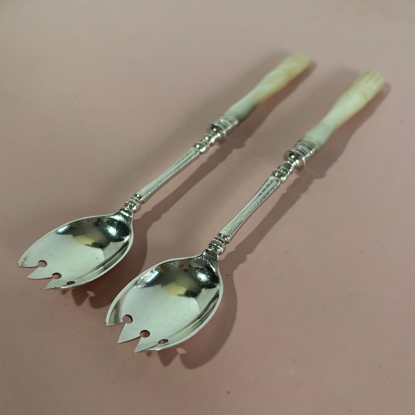 Pair of silver salad servers with decorative handles on a pink background