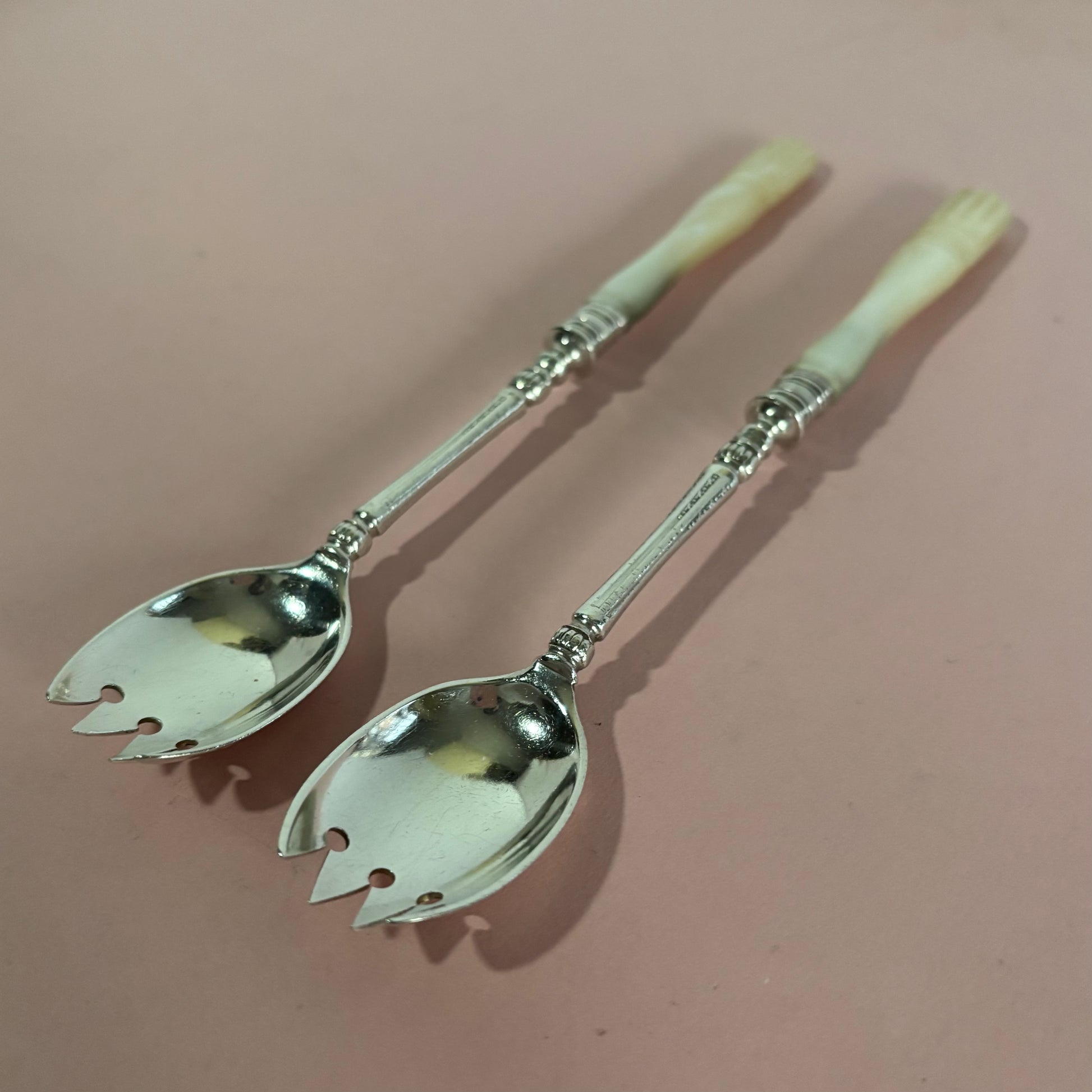 Pair of silver salad servers with decorative handles on a pink background