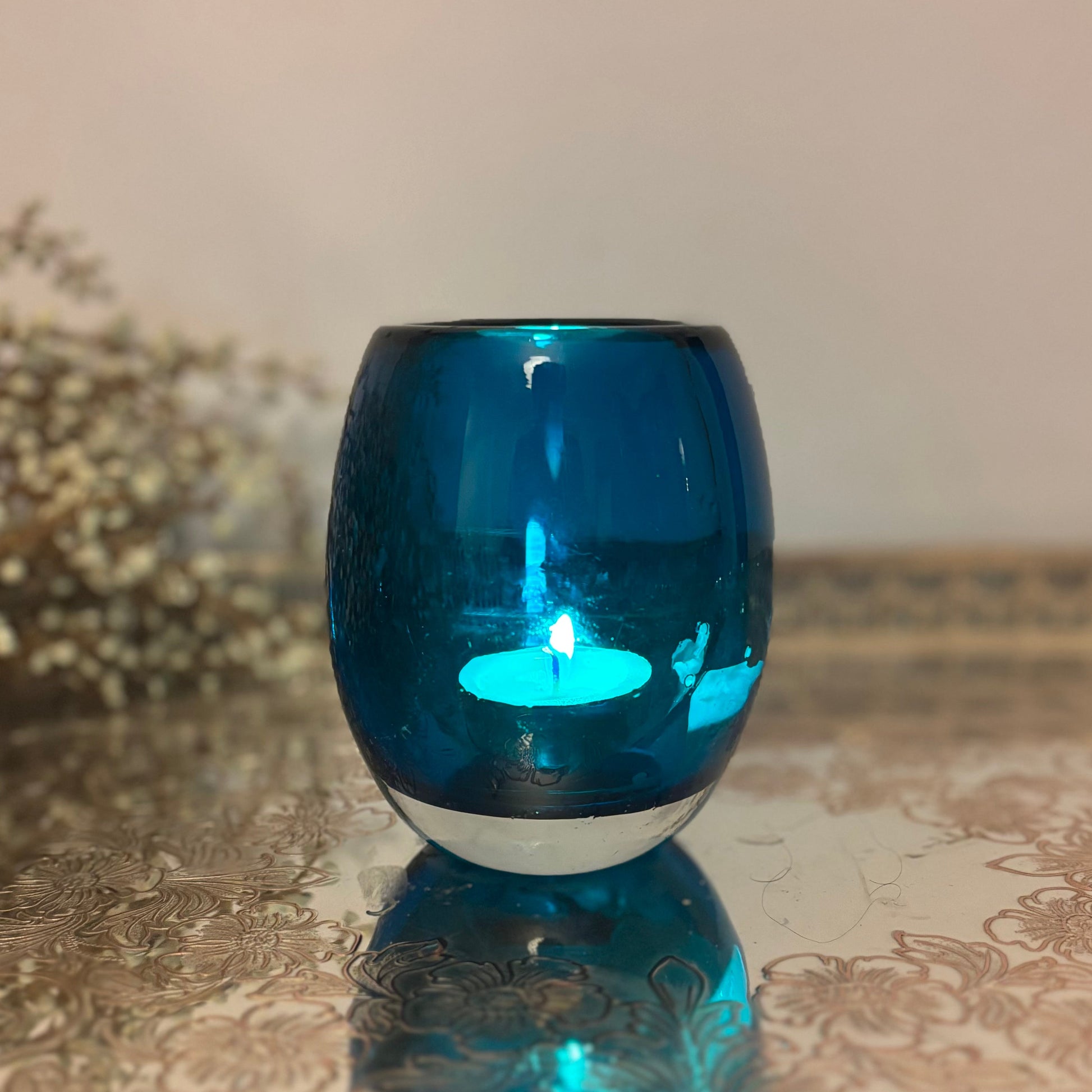 Blue glass candle holder with a lit candle on a reflective surface