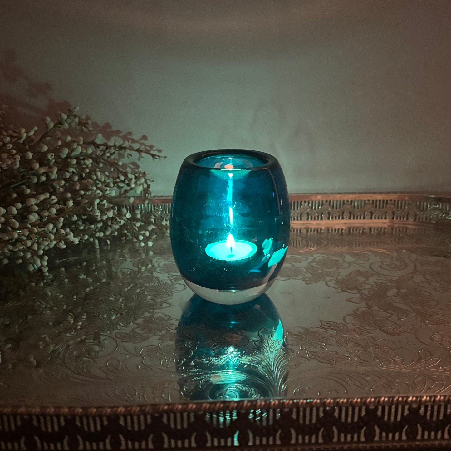 Blue glass candle holder with a candle on a reflective surface