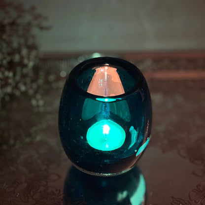 Blue glass candle holder with a lit tealight on a reflective surface