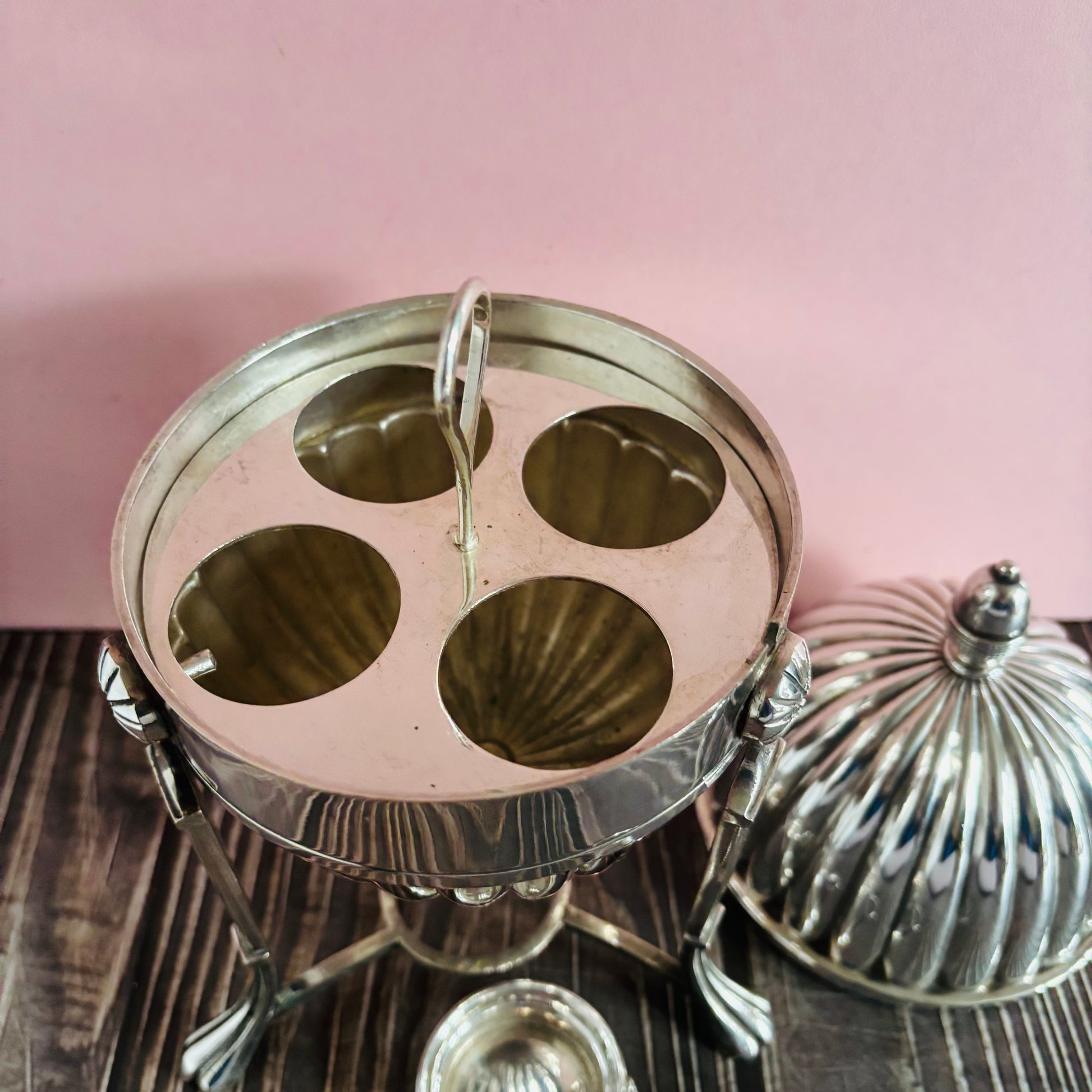 Metallic dome-shaped containers on a wooden surface with a pink background