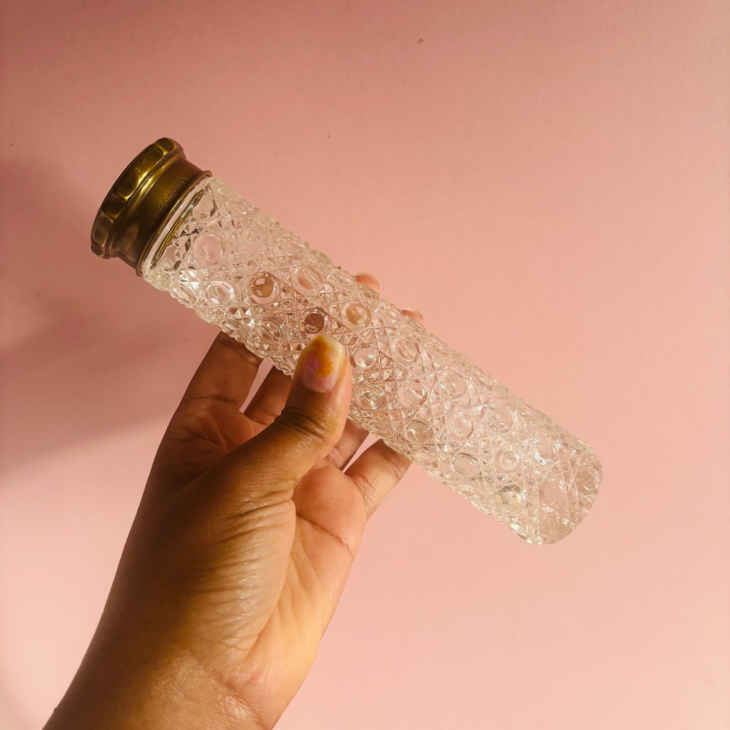 Hand holding a decorative glass bottle with a gold cap against a pink background