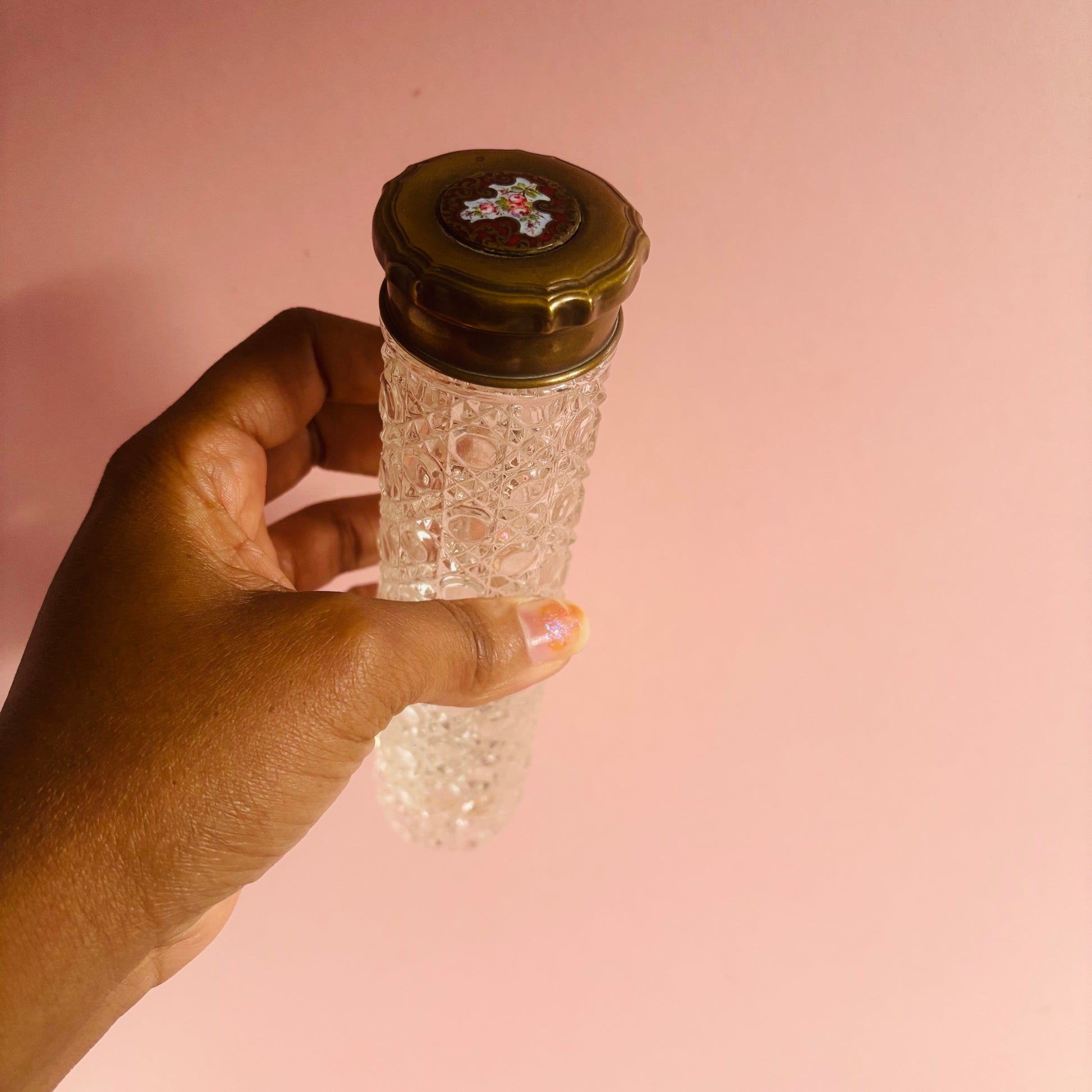 Hand holding a decorative glass bottle with a textured design against a pink background