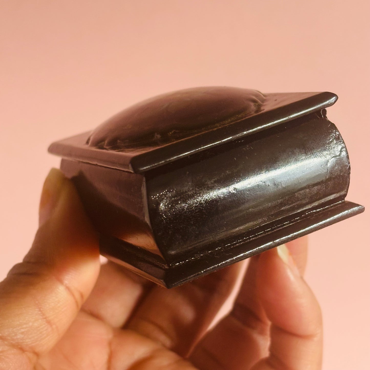 Hand holding a small black leather box against a pink background