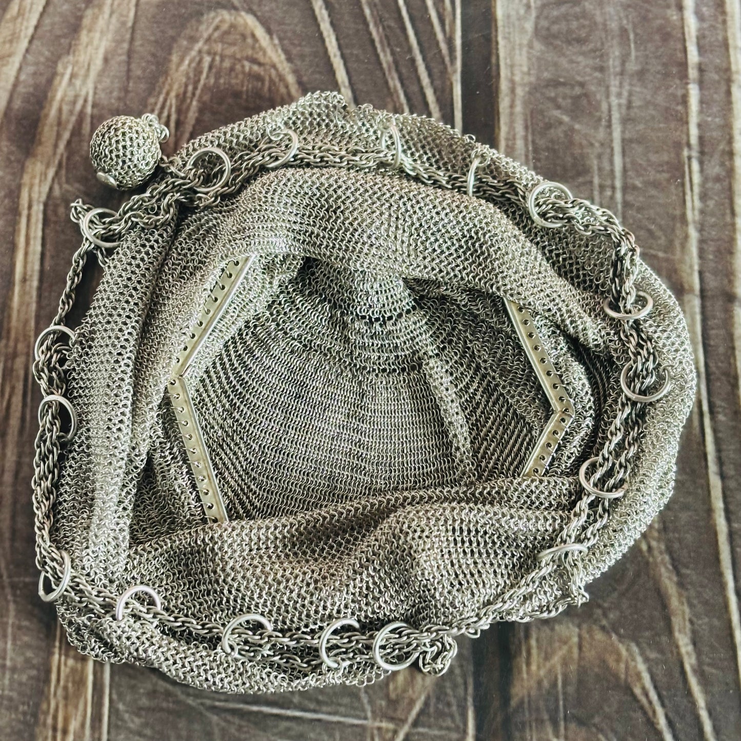 Decorative metal mesh bag with chain details on a wooden surface