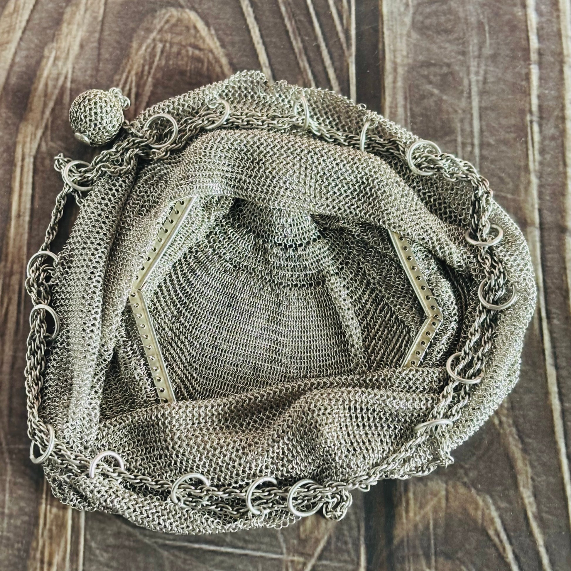 Decorative metal mesh bag with chain details on a wooden surface