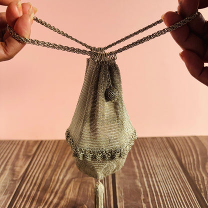Handmade silver mesh bag with chain handle held by hands on a wooden surface with pink background