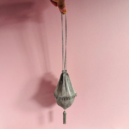 Handbag with chain strap held against a pink background