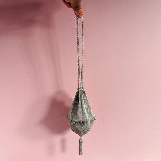 Handbag with chain strap held against a pink background