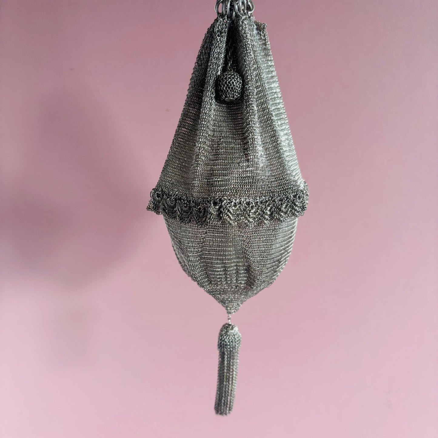 Decorative silver mesh bag with tassel on a pink background
