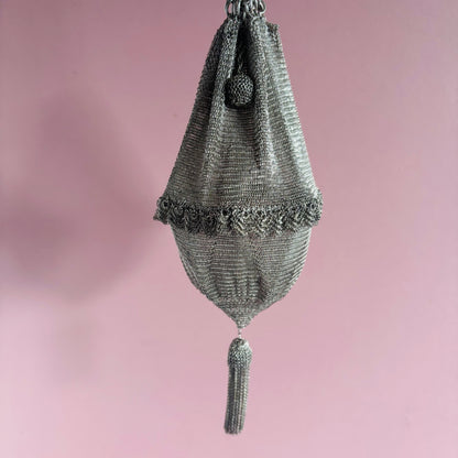 Decorative silver mesh bag with tassel on a pink background